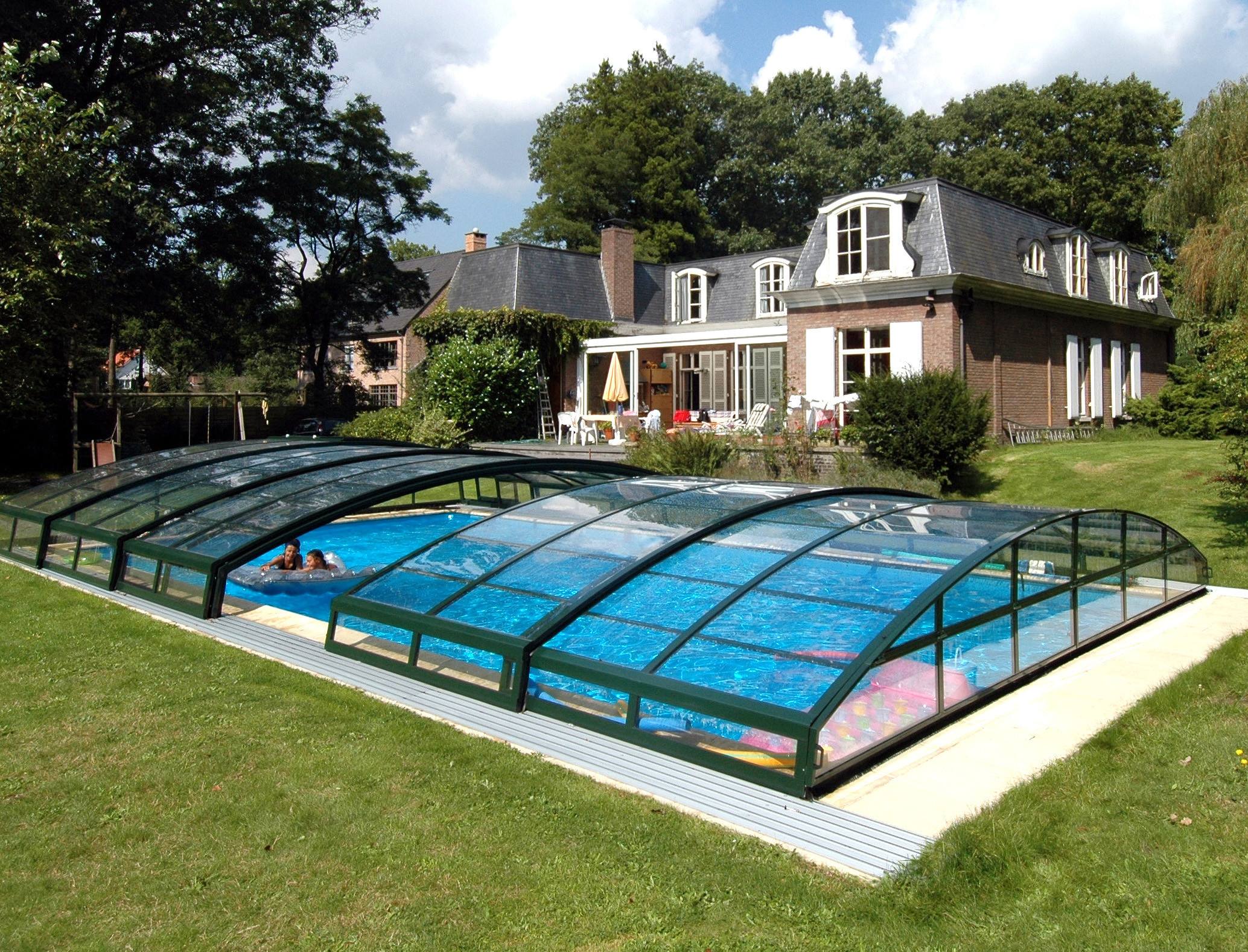 Maison avec piscine couverte et jardin verdoyant.