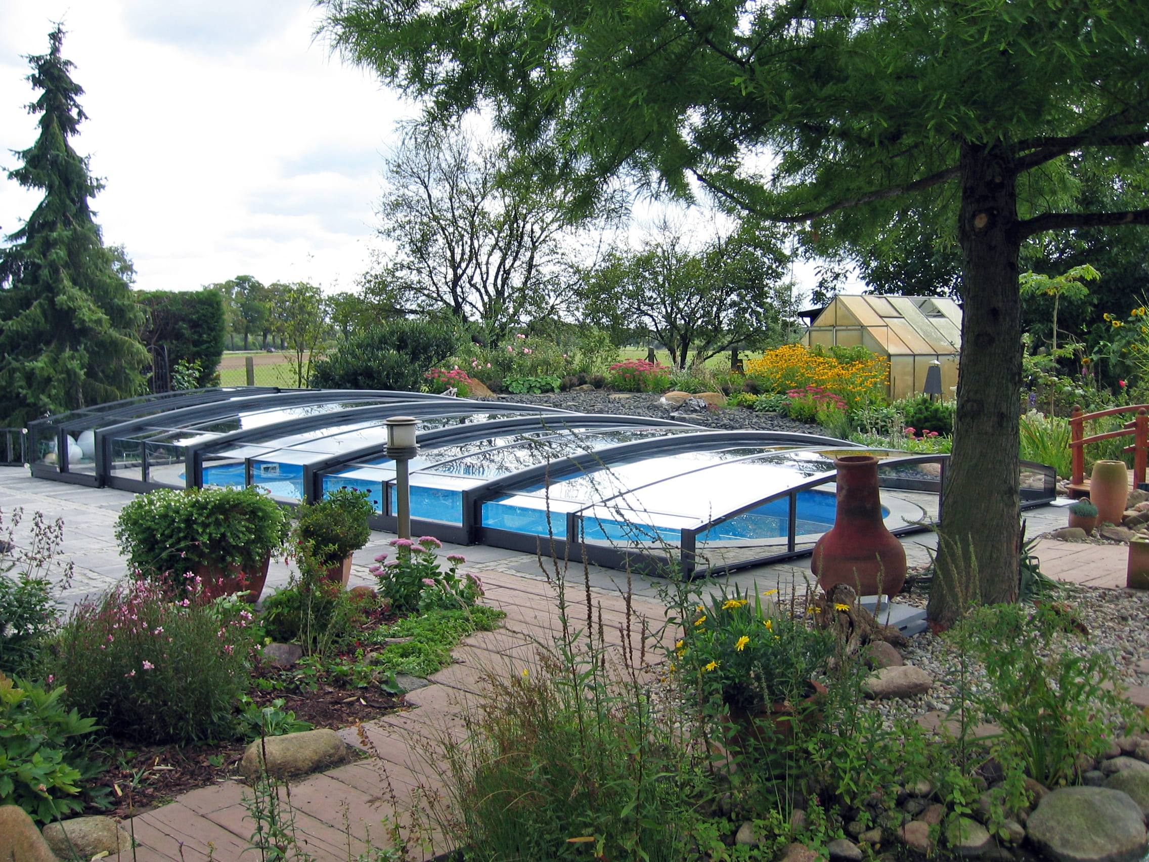 Jardin fleuri avec piscine couverte et serre.